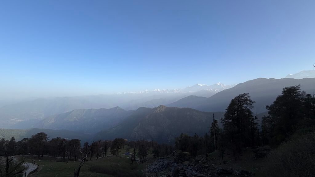 A quiet Himalayan valley and forest beneath a clear blue morning sky