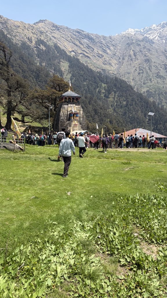 Madhyamaheshwar temple rising above green meadows with forested ridges behind