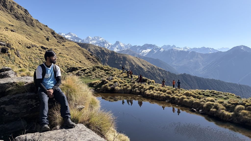 Sitting beside a high-altitude tarn with snow peaks on the Rudranath trail