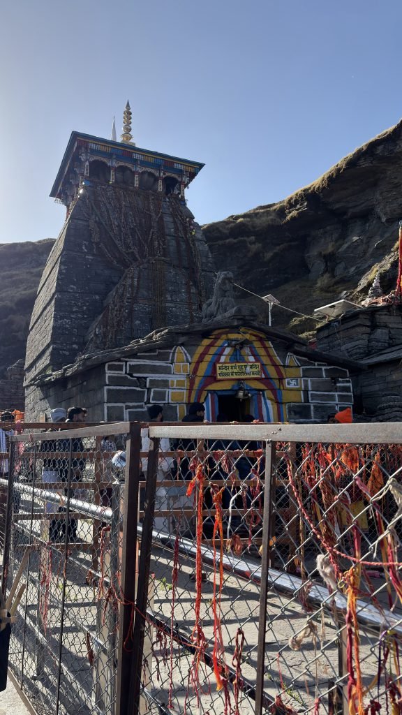 Stone Tungnath temple with red and yellow sacred threads against a blue mountain sky